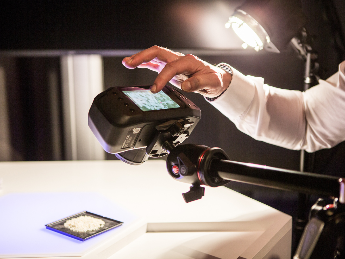 Specim IQ in use attached to a tripod over a sample of rice. Use is navigating data on built-in touchscreen